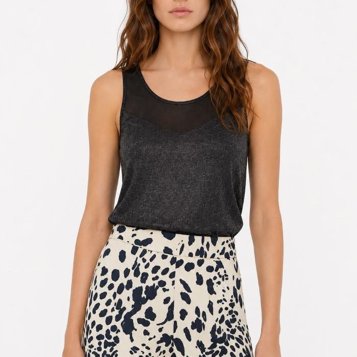 Modelo con top negro Belleza de Malala con transparencias y tejido lúrex brillante combinado con pantalón estampado fluido.
